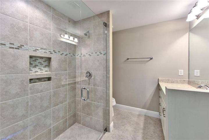 Primary bathroom with tiled shower, shower niche, and quartz countertops