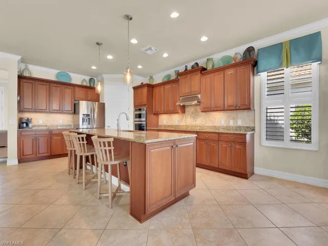 Kitchen with crown molding, light tile patterned floors, a kitchen island with sink, and appliances with stainless steel finishes