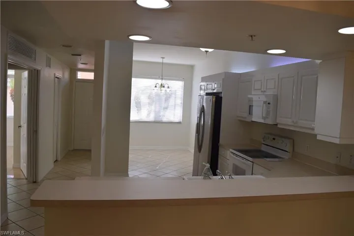 Kitchen featuring white cabinetry, white appliances, light countertops, light tile patterned flooring, and hanging light fixtures