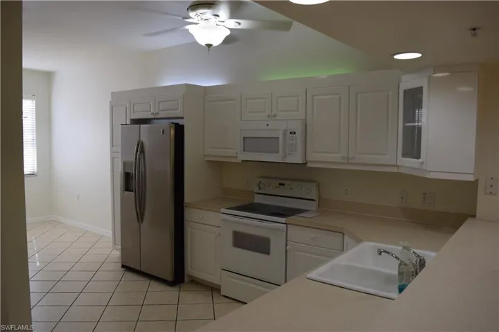 Kitchen with white appliances, light countertops, a ceiling fan, light tile patterned floors, and white cabinets