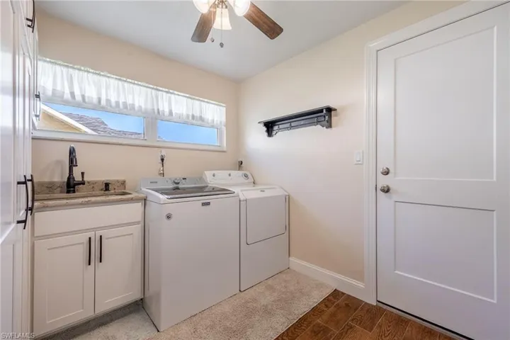 Washroom with light wood-style flooring, ceiling fan, cabinet space, a sink, and washing machine and dryer