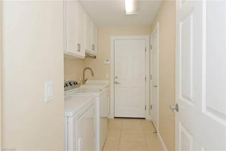 Clothes washing area with cabinets, light tile patterned flooring, sink, and washing machine and dryer