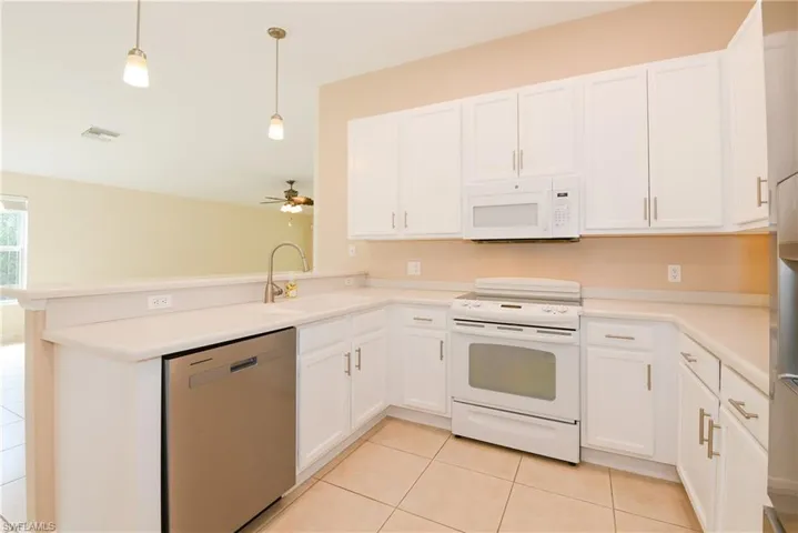 Kitchen featuring kitchen peninsula, white cabinetry, sink, decorative light fixtures, and white appliances