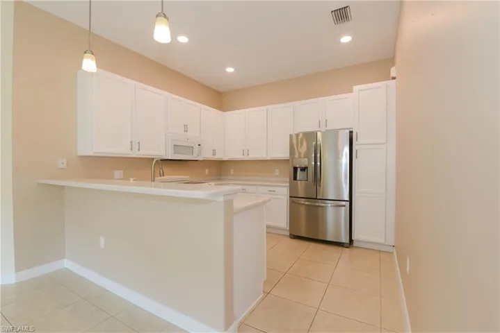 Kitchen with hanging light fixtures, kitchen peninsula, light tile patterned floors, white cabinetry, and white appliances