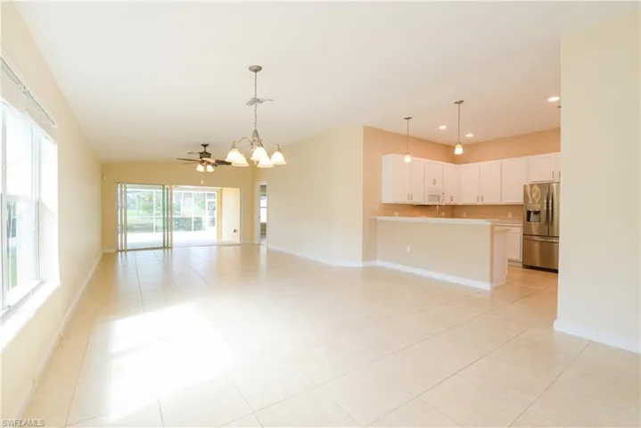 Unfurnished living room featuring lofted ceiling, light tile patterned flooring, and ceiling fan with notable chandelier
