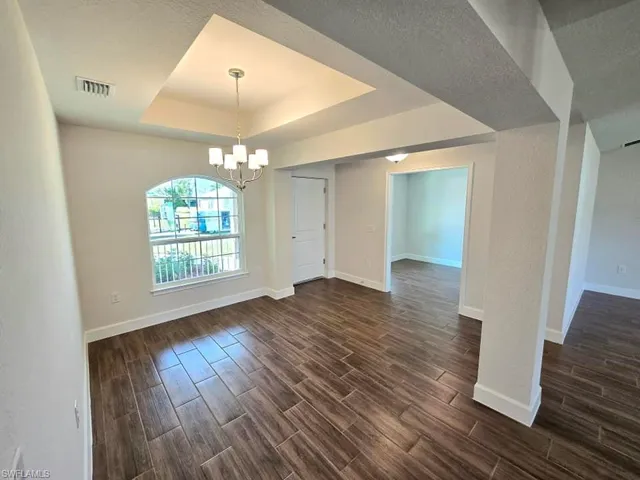 Unfurnished dining area featuring dark wood-type flooring, a textured ceiling, a tray ceiling, and an inviting chandelier