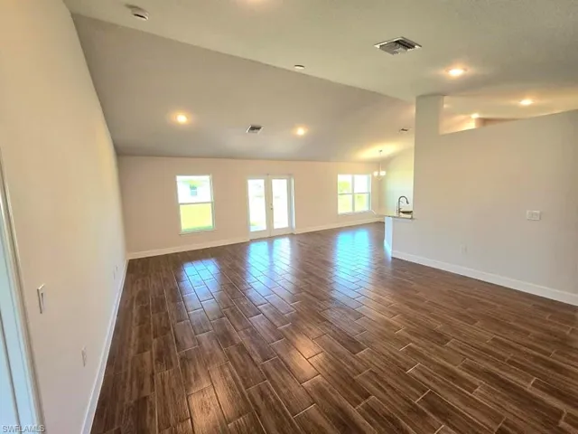 Unfurnished room with dark wood-type flooring, vaulted ceiling, and a notable chandelier