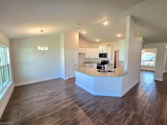 Kitchen with light stone countertops, vaulted ceiling, white cabinets, appliances with stainless steel finishes, and dark hardwood / wood-style flooring