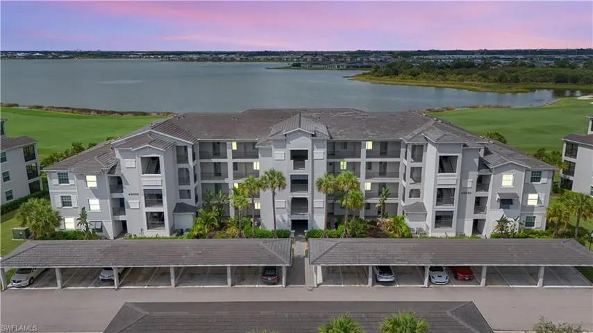 Multi-story residential building featuring balconies, covered parking structures, and mature palm trees
