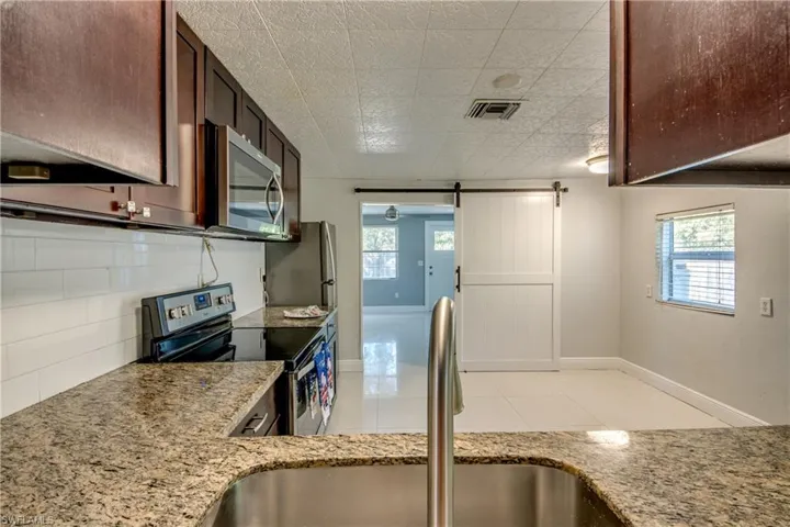 Kitchen featuring a barn door, appliances with stainless steel finishes, backsplash, and light stone counters