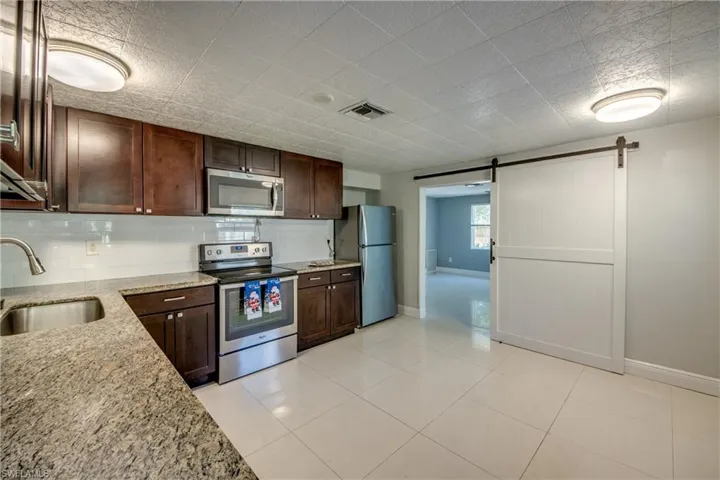 Kitchen featuring a barn door, dark brown cabinetry, stainless steel appliances, and light stone counters