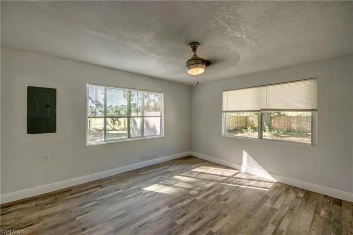 Unfurnished room featuring a textured ceiling, electric panel, wood finished floors, and ceiling fan