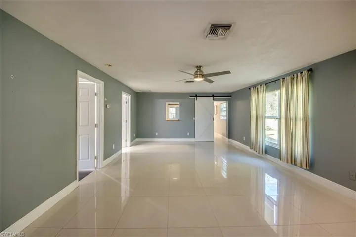 Unfurnished room featuring a barn door, a ceiling fan, and light tile patterned flooring