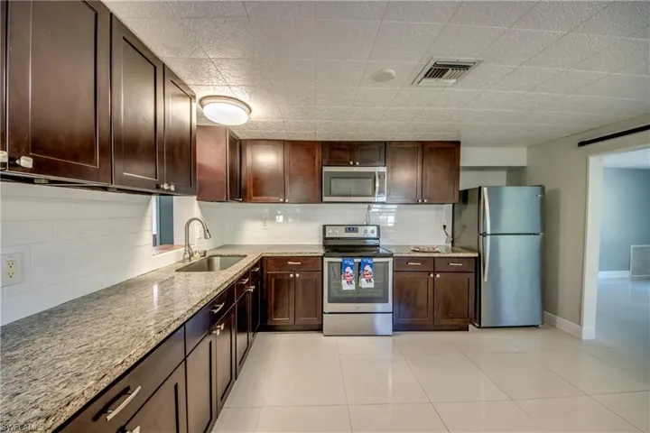 Kitchen with stainless steel appliances, dark brown cabinetry, light stone counters, and tasteful backsplash