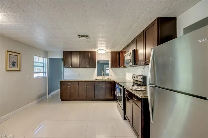 Kitchen with appliances with stainless steel finishes, dark brown cabinets, light tile patterned floors, and decorative backsplash