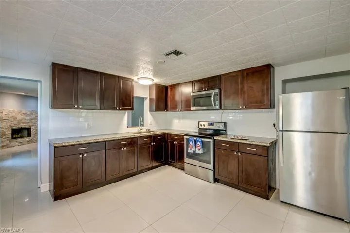 Kitchen featuring appliances with stainless steel finishes, dark brown cabinetry, a fireplace, and light tile patterned floors