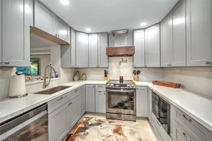 Kitchen featuring gray cabinetry, a sink, stainless steel appliances, wall chimney exhaust hood, and decorative backsplash