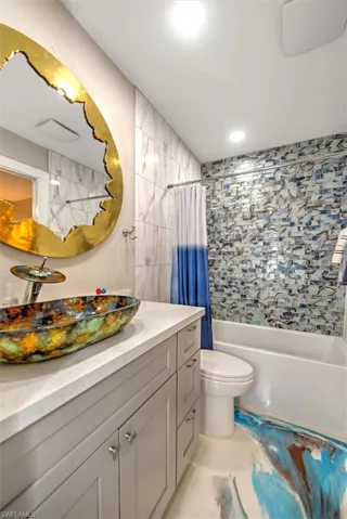 Bathroom featuring shower / bathtub combination with curtain, toilet, and vanity