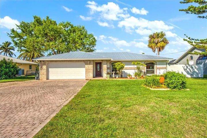 Single story home featuring brick siding, fence, metal roof, decorative driveway, and an attached garage