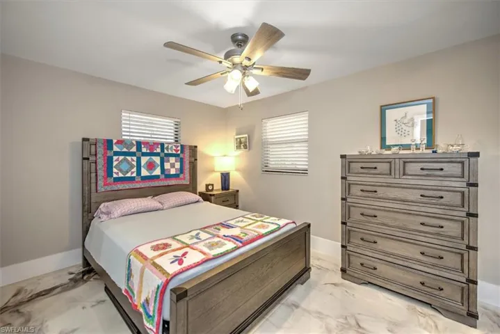 Bedroom featuring multiple windows, baseboards, marble finish floor, and ceiling fan