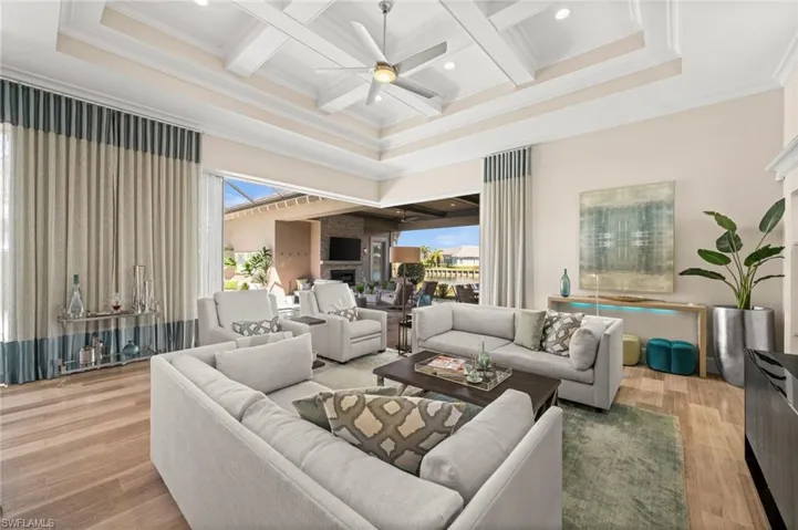Living room with coffered ceiling, beamed ceiling, a ceiling fan, a high ceiling, and light wood-style flooring