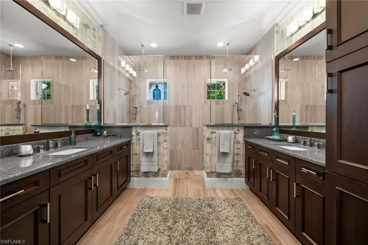 Full bath featuring tile walls, two vanities, a stall shower, and light wood-style flooring