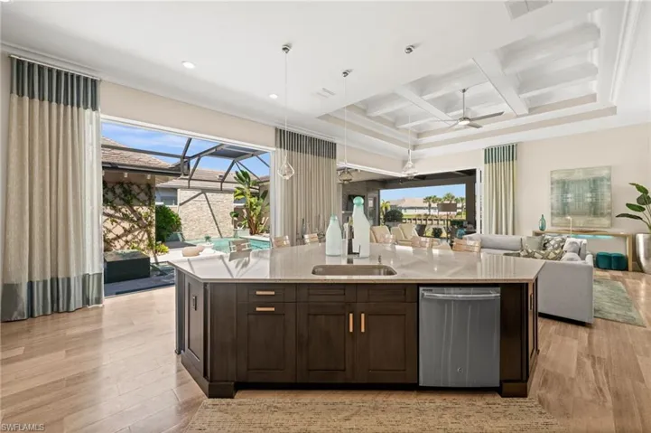 Kitchen featuring open floor plan, dark brown cabinetry, stainless steel dishwasher, coffered ceiling, and light stone counters