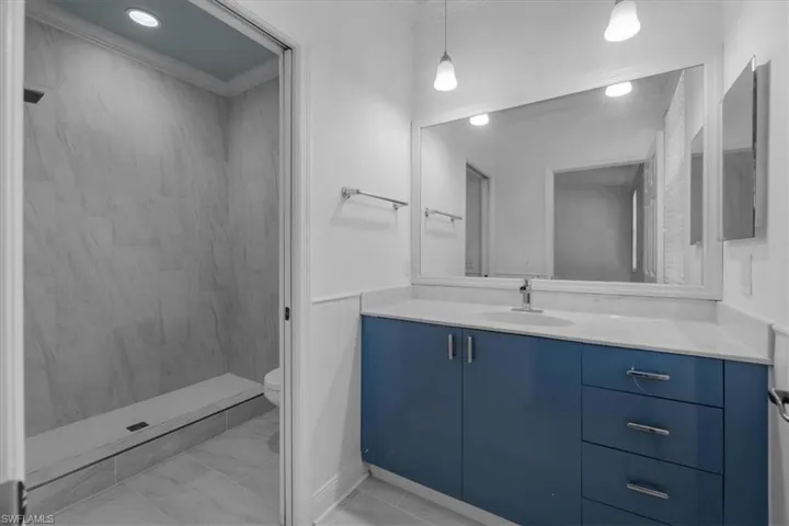 Bathroom with vanity, toilet, ornamental molding, and tiled shower