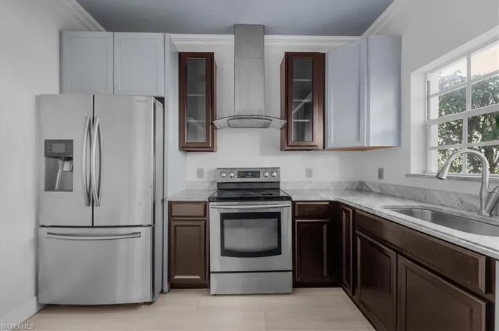Kitchen featuring sink, stainless steel appliances, wall chimney range hood, and ornamental molding