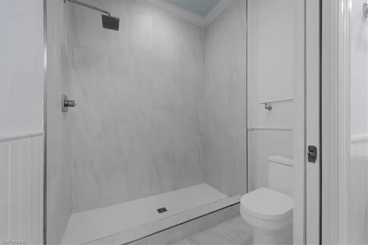 Bathroom featuring crown molding, toilet, and tiled shower