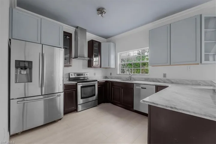 Kitchen featuring appliances with stainless steel finishes, sink, ornamental molding, and wall chimney range hood