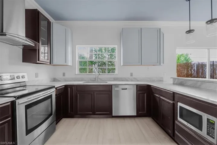 Kitchen featuring hanging light fixtures, sink, wall chimney exhaust hood, light wood-type flooring, and appliances with stainless steel finishes