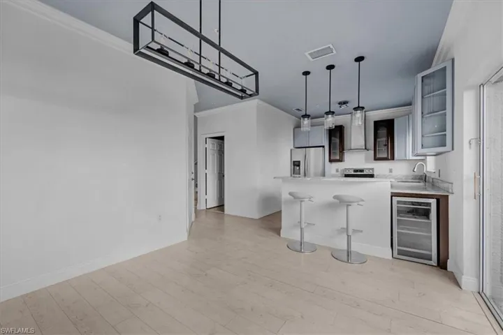 Kitchen featuring kitchen peninsula, light wood-type flooring, stainless steel appliances, and beverage cooler