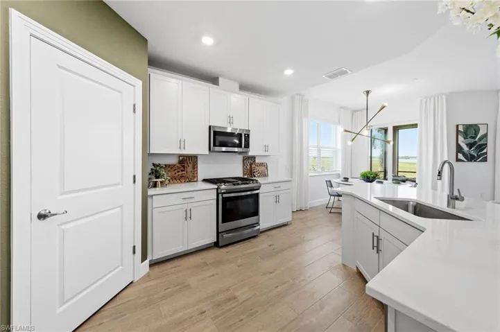 White cabinetry with stainless steel appliances, wood-finish flooring, and light-toned countertops