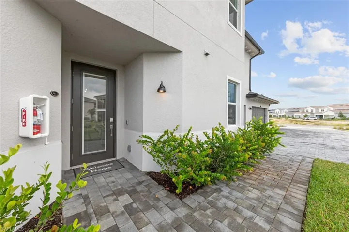 Stucco exterior with a glass-paneled entry door, a paver walkway, decorative outdoor lighting, and established shrubbery