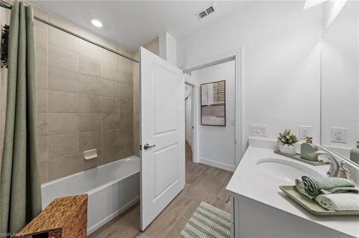 Full bathroom featuring a white tub with tile surround, wood-finish flooring, a single vanity with a white countertop, and an integrated sink