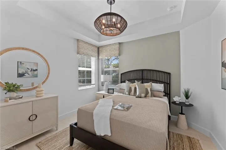 Tray ceiling with a central woven chandelier, dual windows featuring blinds and valances, and wood-finish flooring