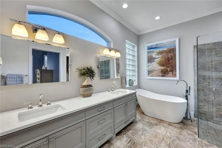 Bathroom featuring dual sinks, tile flooring, crown molding, shower with separate bathtub, and large vanity