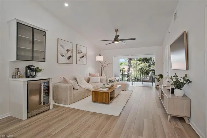 Living room featuring light wood-type flooring, a ceiling fan, vaulted ceiling, beverage cooler, and a bar