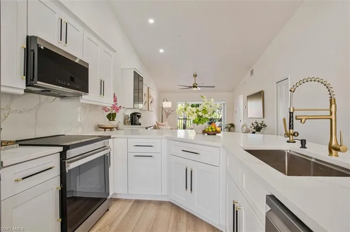 Kitchen with stainless steel appliances, white cabinetry, lofted ceiling, light stone countertops, and light wood-style floors