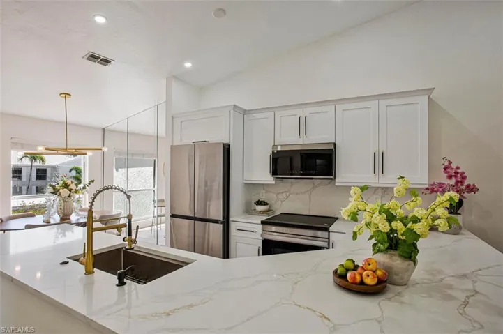 Kitchen featuring light stone counters, stainless steel appliances, white cabinets, vaulted ceiling, and decorative backsplash