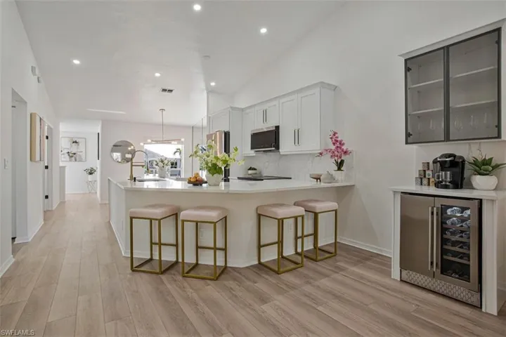 Kitchen with beverage cooler, a breakfast bar, a peninsula, light wood-style floors, and vaulted ceiling