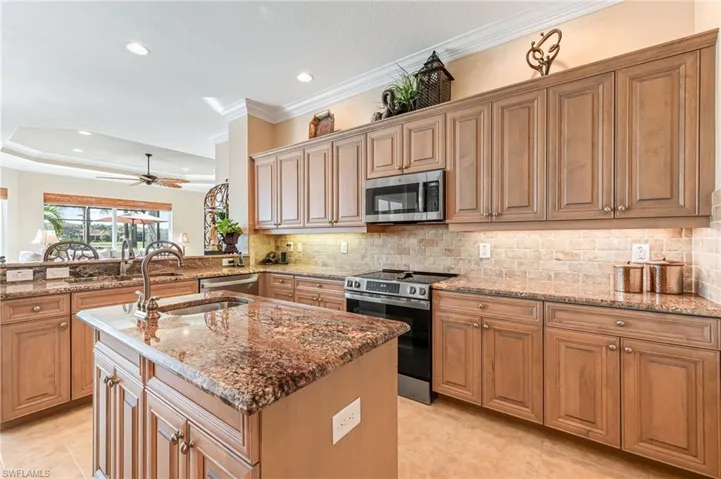 Kitchen with light stone countertops, kitchen peninsula, stainless steel appliances, crown molding, and a center island with sink
