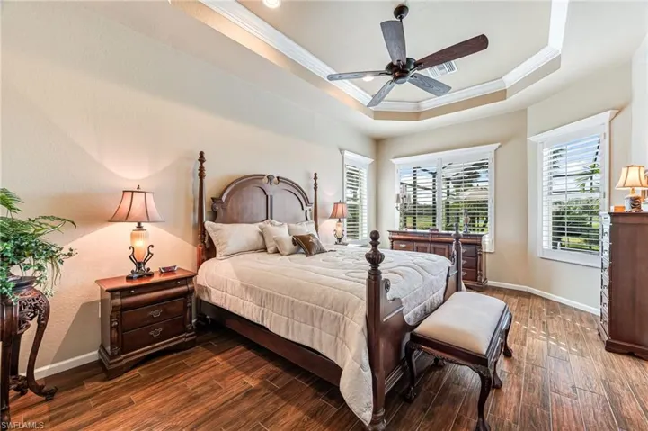 Bedroom with dark wood-type flooring, a raised ceiling, crown molding, and ceiling fan