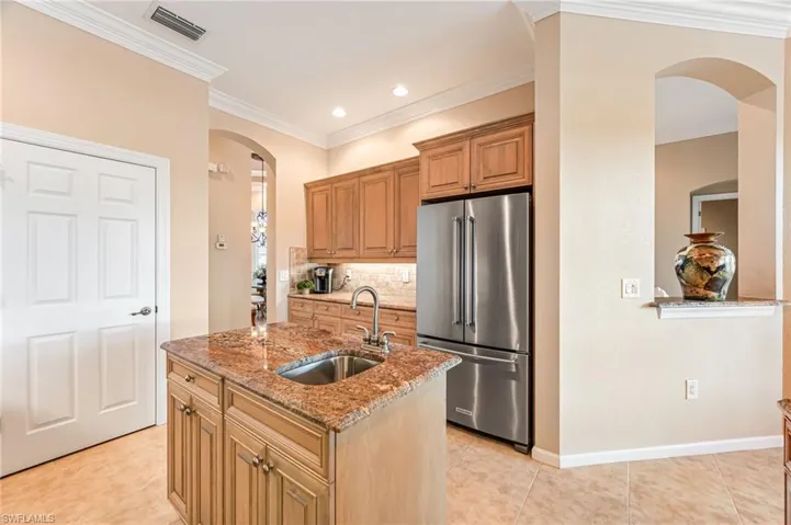 Kitchen featuring high end refrigerator, decorative backsplash, a center island with sink, sink, and light stone countertops