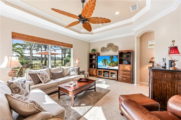 Living room with ornamental molding, light tile patterned flooring, a tray ceiling, and ceiling fan