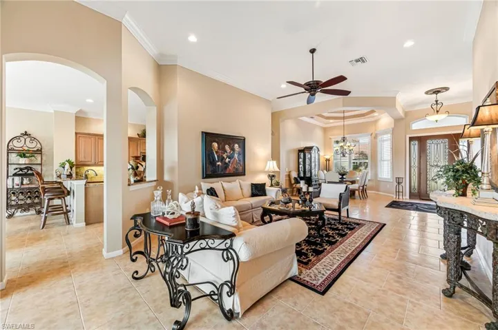 Tiled living room with crown molding and ceiling fan with notable chandelier
