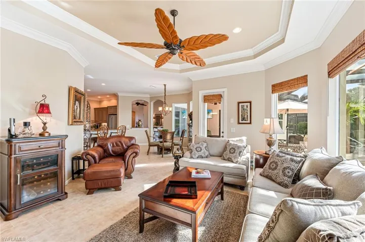 Living room featuring crown molding, light tile patterned flooring, a tray ceiling, and ceiling fan with notable chandelier