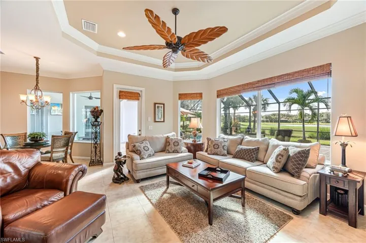 Tiled living room with ornamental molding, ceiling fan with notable chandelier, and a raised ceiling