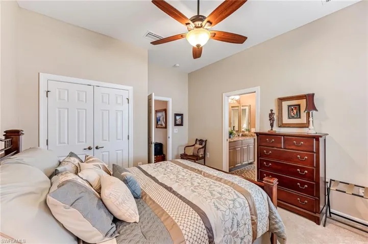 Bedroom with a closet, ceiling fan, light carpet, and connected bathroom